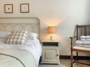 Un letto con testiera, un comodino con una lampada, una sedia con degli asciugamani e due quadri appesi al muro.
