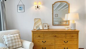 Un dormitorio con un aparador de madera, un espejo, lámparas de noche, un cuadro enmarcado y una almohada a cuadros.