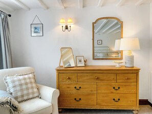 Une chambre à coucher avec une commode en bois, un miroir, des lampes de chevet, un tableau encadré et un coussin à carreaux.