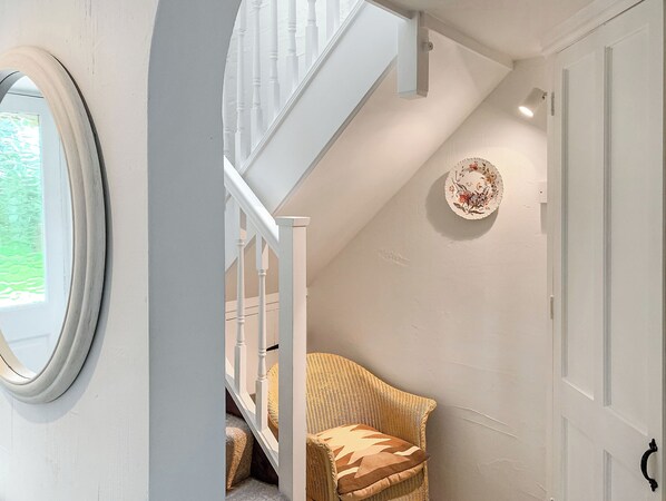 A staircase with white balusters, a wicker chair with a cushion, a decorative plate on the wall, and a door with a handle.