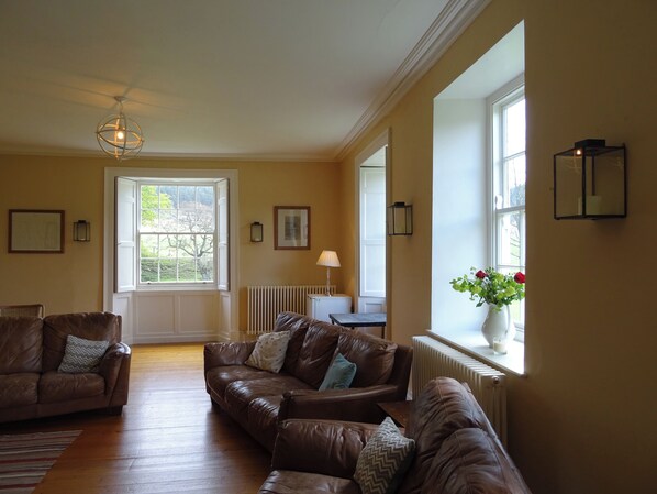 A spacious living room with leather sofas, a radiator, a table with a lamp, and a large window with a view.