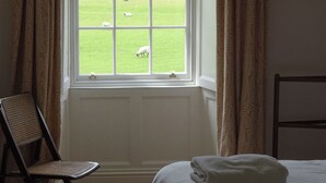 Een kamer met een groot raam, een bed, een stoel en een houten kapstok aan de muur.