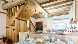Une cuisine avec des poutres en bois, une table à manger recouverte d’une nappe à pois et un escalier.