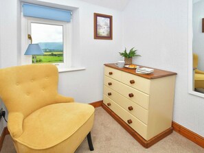 A room with a yellow armchair, a wooden dresser with drawers, a window with a view of green fields, and a framed picture on the wall. - 2 bedroom accommodation in Bassenthwaite, near Keswick (Bassenthwaite, near Keswick)