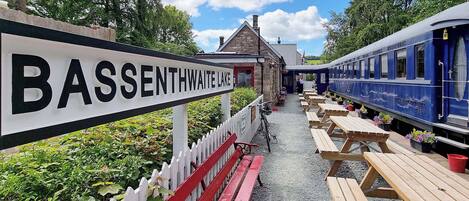A sign for BASSENTHWAIT LAKE, a wooden bench-lined pathway, and a blue train with a dining car.