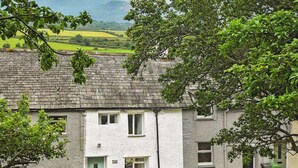 A white house with a stone roof, a green door, and a small garden with two wooden chairs and a table. - 2 bedroom accommodation in Bassenthwaite, near Keswick (Bassenthwaite, near Keswick)