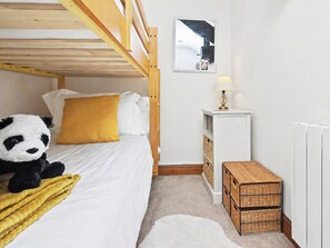 A bedroom with a bunk bed, a bedside table with a lamp, a wicker storage unit, and a stuffed panda toy.