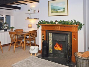 A cozy living room with a fireplace, a dining table with chairs, a small white dog, and a Christmas tree. - 2 bedroom accommodation in Bassenthwaite, near Keswick (Bassenthwaite, near Keswick)