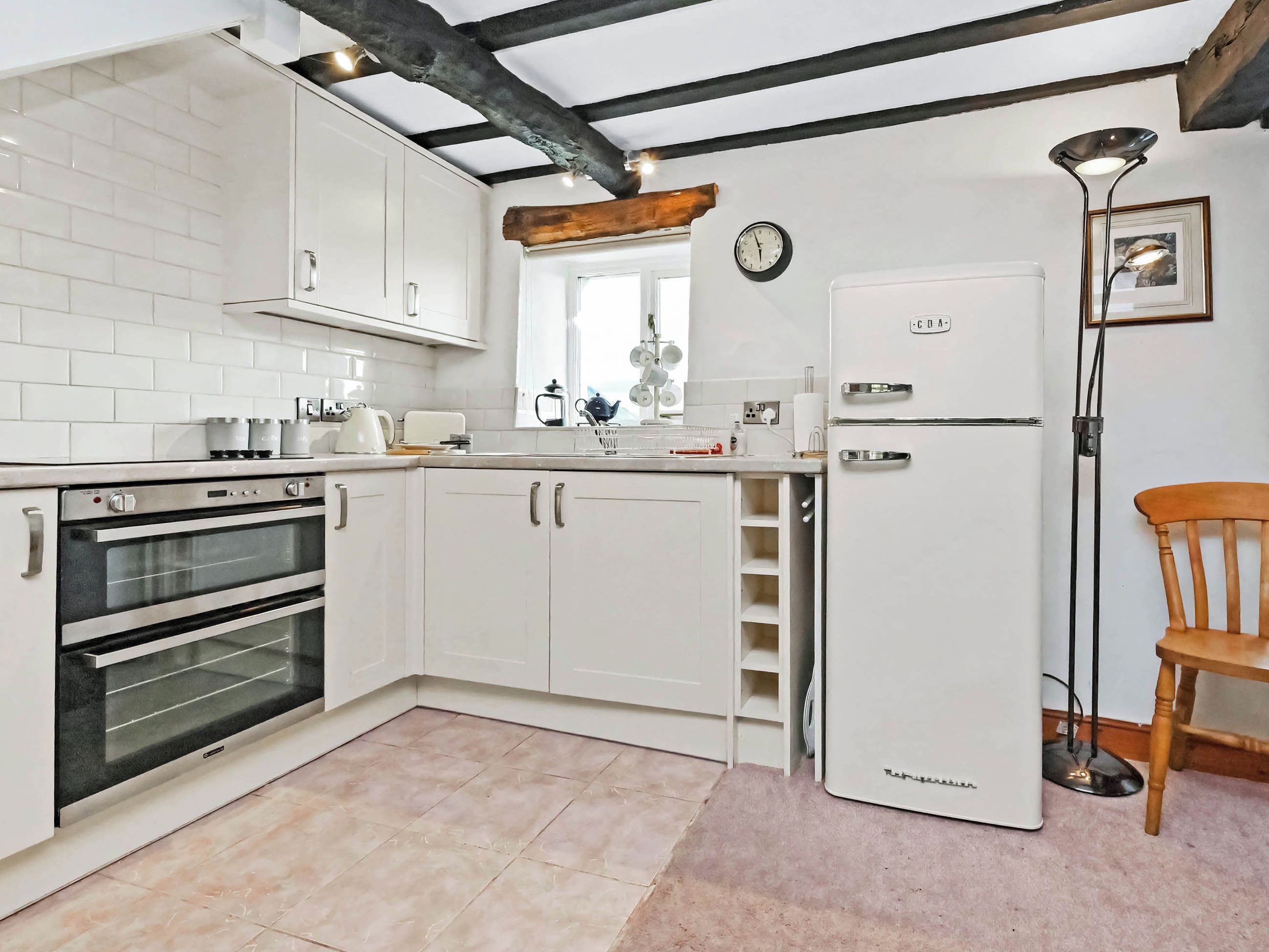 Une cuisine moderne avec des meubles blancs, un four encastré, un réfrigérateur et un plafond avec une poutre en bois.
