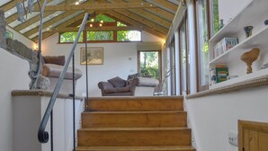 Un escalier en bois mène à une mezzanine dotée d’un plafond en pente, d’un banc rembourré et d’une bibliothèque agrémentée d’objets décoratifs.