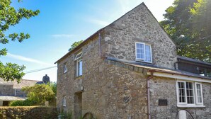 Une maison en pierre avec un toit en pente, un petit porche et un jardin fleuri.