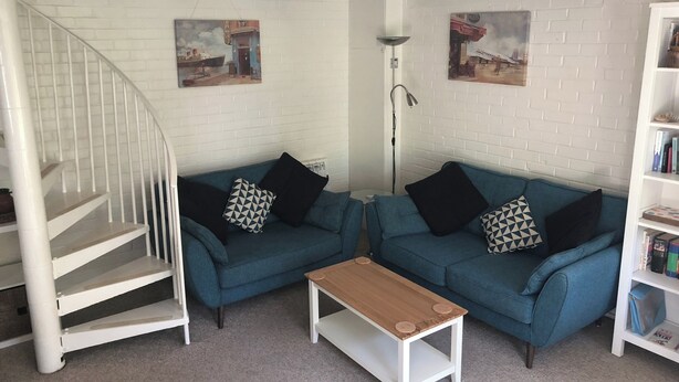 A living room with two blue sofas, a wooden coffee table, a white staircase, and a white brick wall with two paintings.