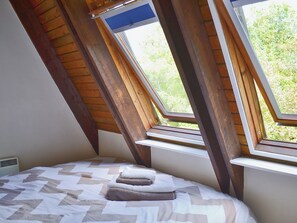 A bedroom with a sloped ceiling, a bed with a patterned bedspread, and a window with a view of greenery.
