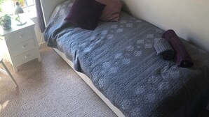 A bedroom with a bed, a nightstand, a lamp, and a window.