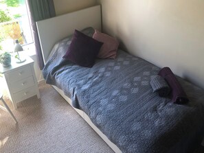 Une chambre à coucher avec un lit, une table de chevet, une lampe et une fenêtre.