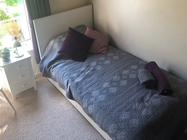 A bedroom with a bed, a nightstand, a lamp, and a window.