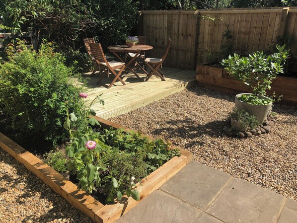 A wooden deck with a table and chairs, surrounded by raised garden beds and a wooden fence.
