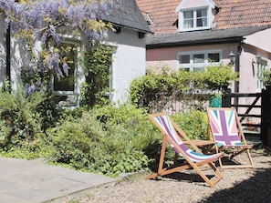 A house with a garden, two wooden beach chairs, and a white fence.