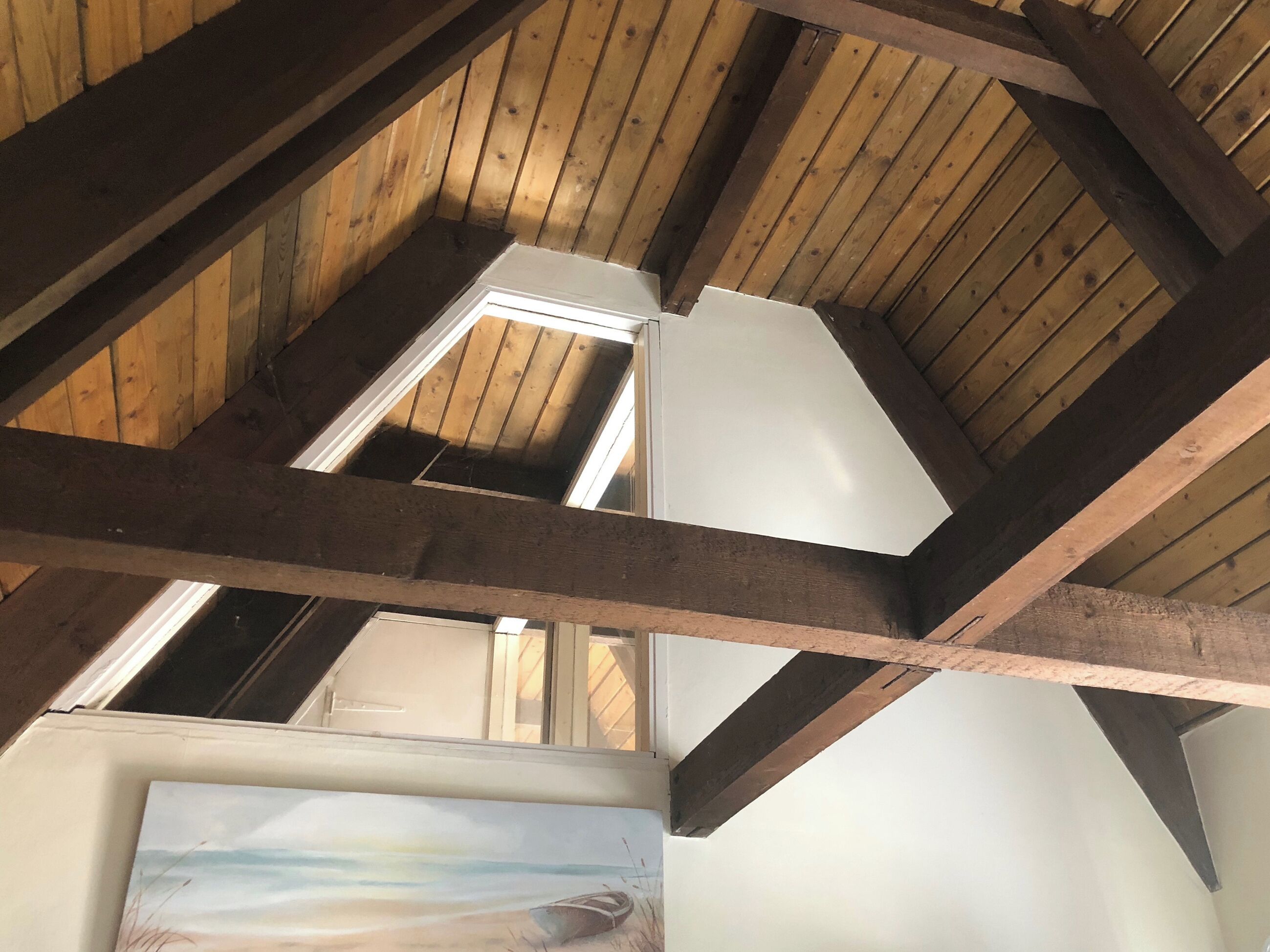 A room with wooden beams, a skylight, and a painting of a beach scene.