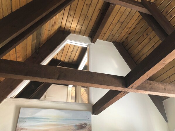 Une pièce avec des poutres en bois, une lucarne et un tableau représentant une scène de plage.