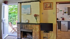 A room with a fireplace, a television, a clock, and a kitchen area.