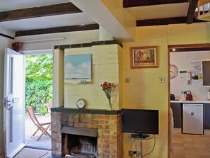 A room with a fireplace, a television, a clock, and a kitchen area.