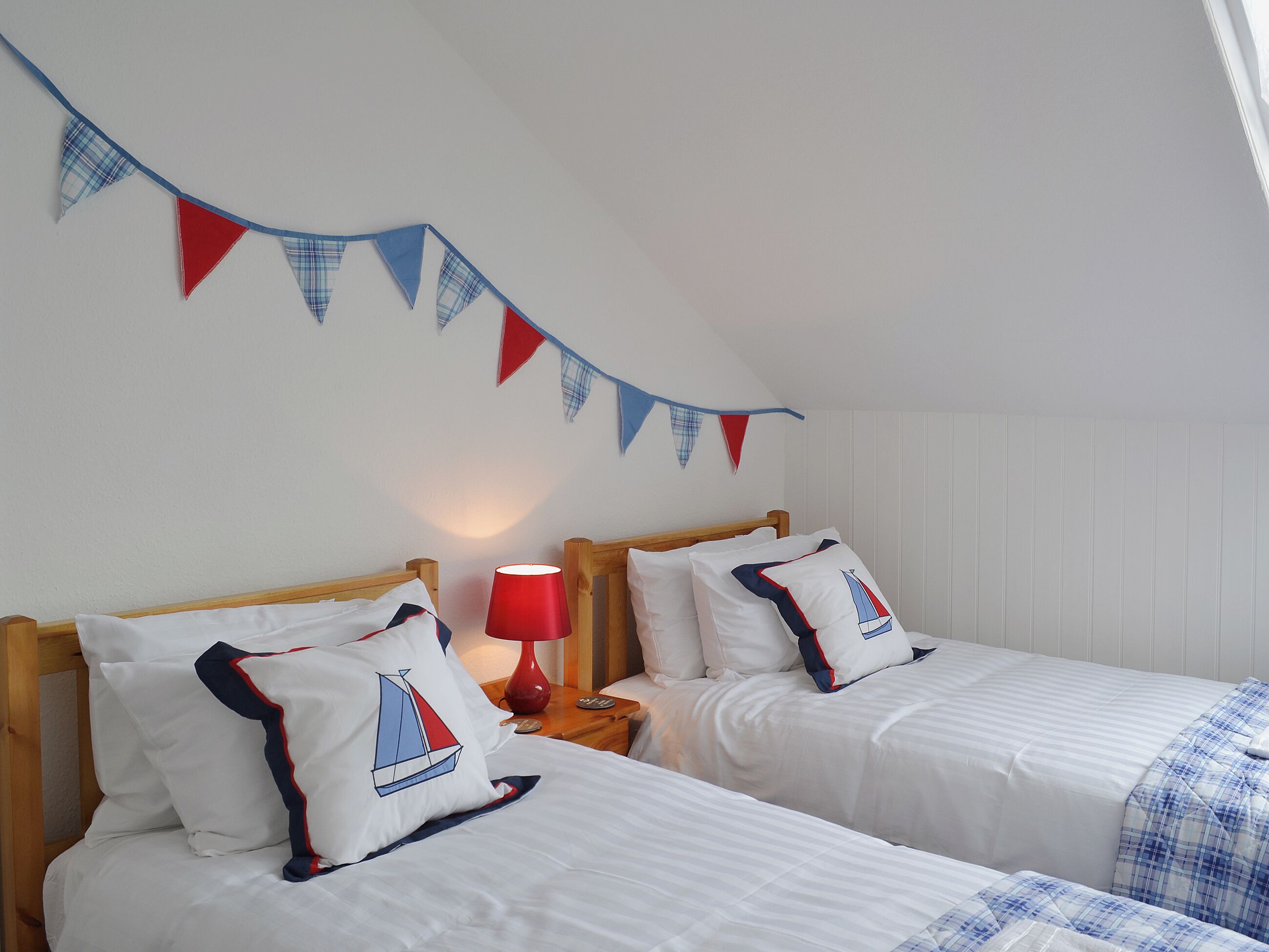 A bedroom with two beds, a red lamp, and bunting on the wall.