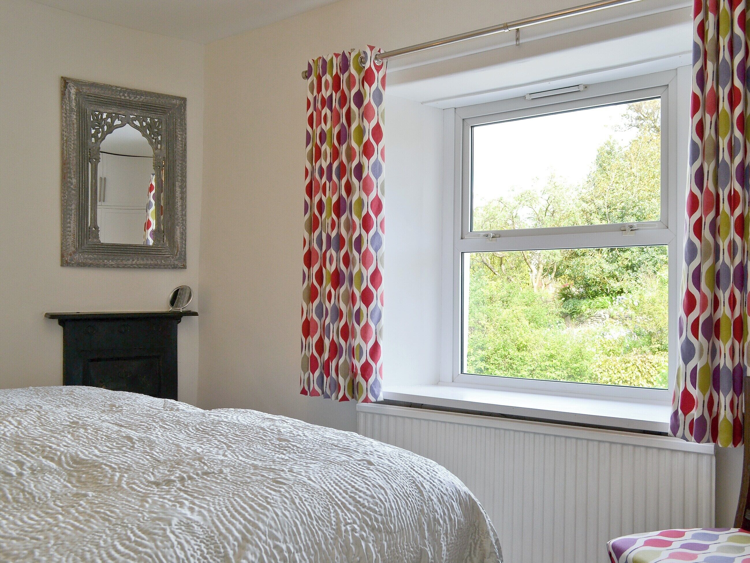 A bedroom with a bed, a dresser, a mirror, and a window with curtains.