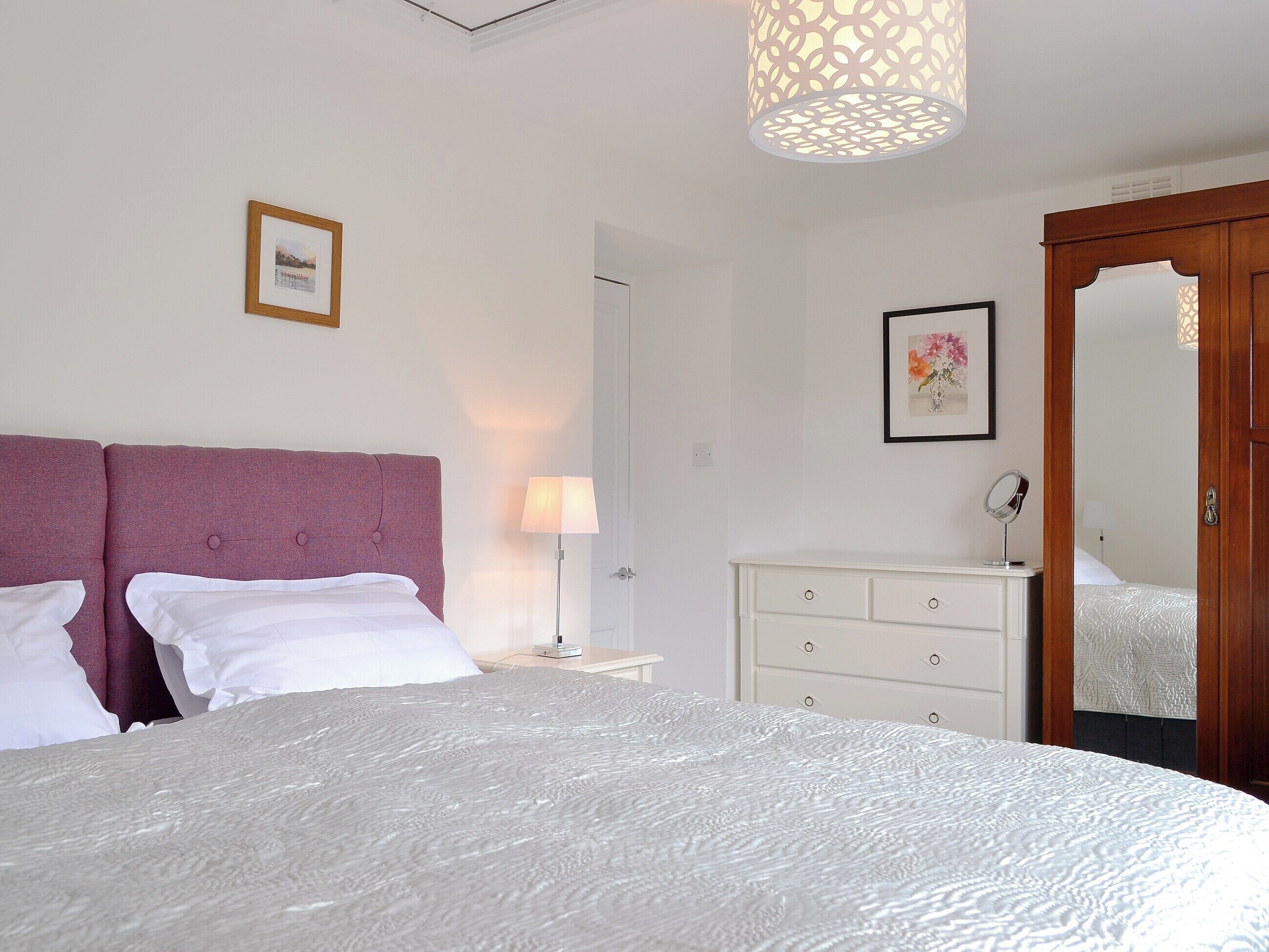 Une chambre à coucher avec un grand lit, une table de chevet, une lampe, une commode et un miroir.