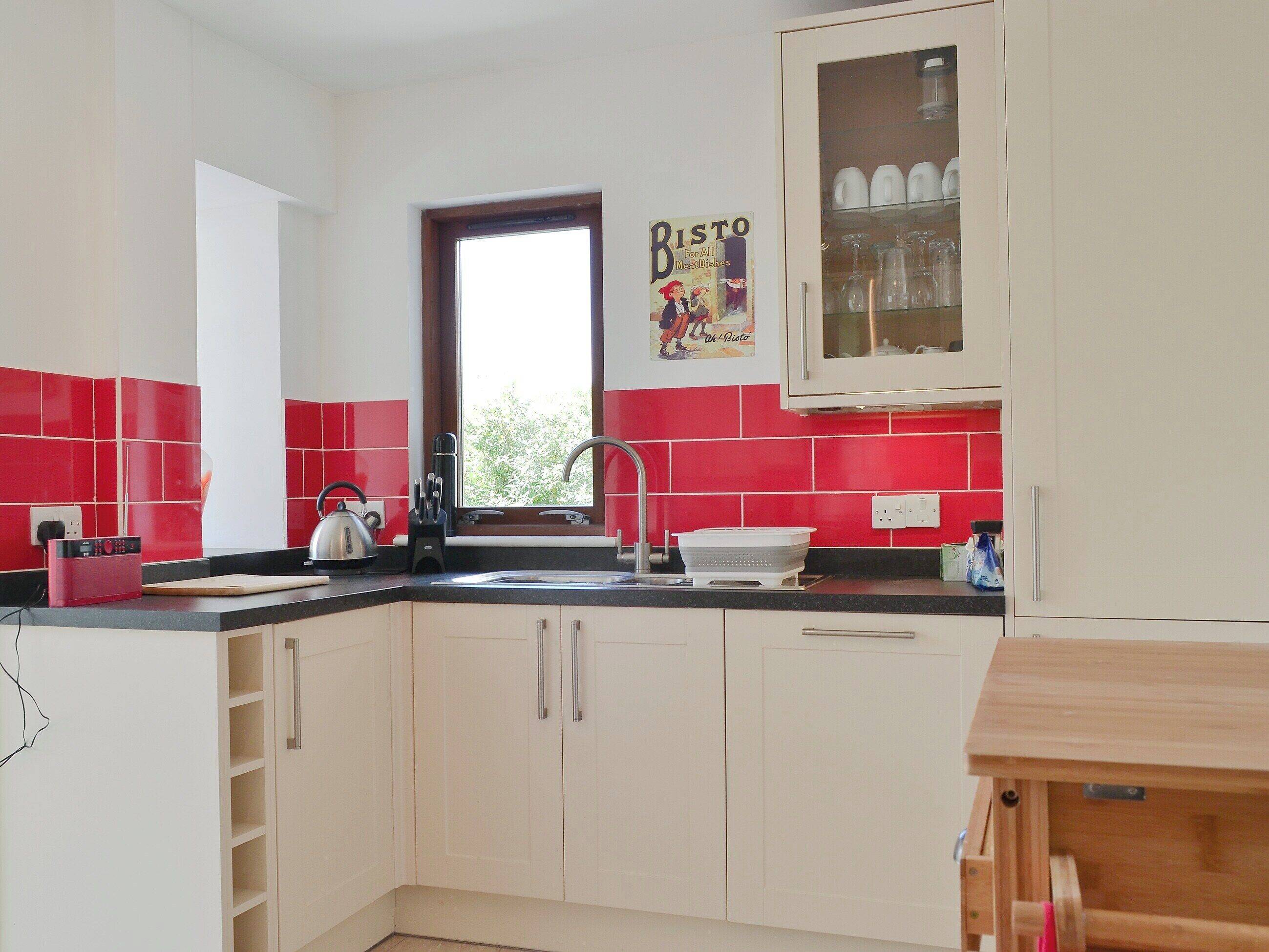 A kitchen with red and white tiles, a sink, cabinets, and a window with a view.