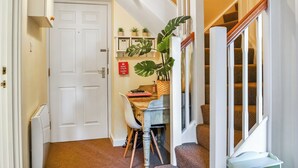 A hallway with a white door, a staircase with wooden railings, and a desk with a chair and a potted plant. - County House Apartment - 27911 (York)