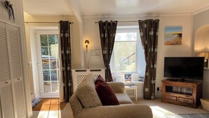 Una sala de estar con un sofá color beige, un televisor sobre un mueble de madera y una ventana con cortinas.