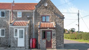 Une petite maison en pierre avec un toit recouvert de tuiles rouges, une petite fenêtre et une porte.