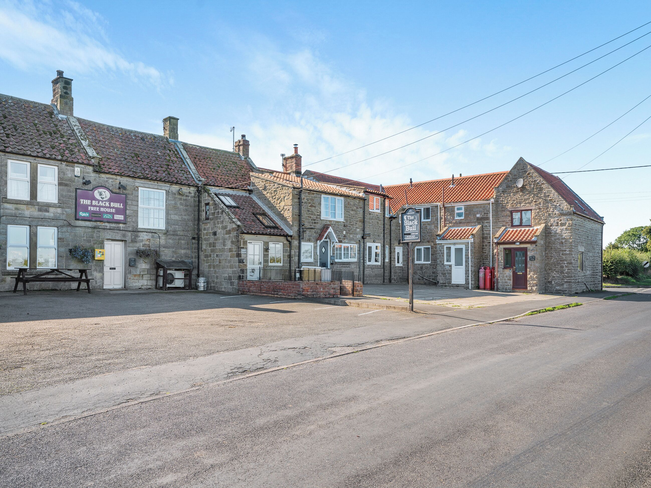 A stone building with a sign for 'The Black Bull Free House' and a bench outside.
