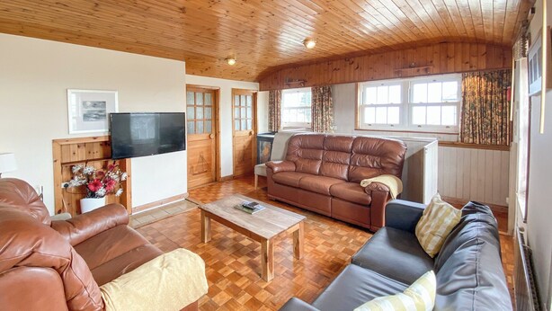 Una sala de estar acogedora con piso de madera, un sofá de cuero marrón, un sofá de cuero negro, una mesa de centro de madera y un televisor en la pared.