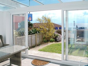 A conservatory with a glass door leading to a garden with a wooden fence, a bench, and a table. - 3 bedroom accommodation in Sandown (Sandown)