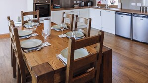A modern kitchen with white cabinets, stainless steel appliances, and a wooden dining table set for six.
