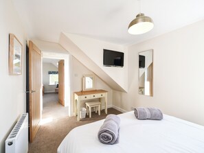 A bedroom with a bed, a desk, a mirror, a TV, and a radiator. - 2 bedroom accommodation in Kirkcudbright (Kirkcudbright)