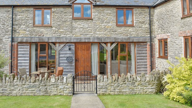 A stone cottage with a wooden front door, large windows, and a stone wall with a gate.