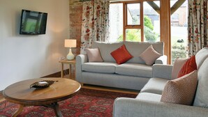 A living room with a grey sofa, patterned cushions, a wooden coffee table, a lamp, and a TV on the wall.