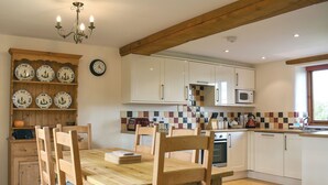 A kitchen with wooden cabinets, a dining table with chairs, a clock, and a tiled backsplash.