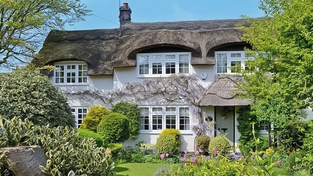 A traditional thatched-roof house with white-framed windows, surrounded by a well-maintained garden with various plants and a wooden fence. - 3 bedroom accommodation in Winterton-on-Sea, near Great Yarmouth (Winterton-on-Sea, near Great Yarmouth)