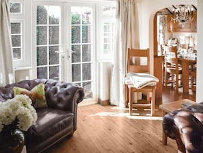 A living room with a leather sofa, a wooden chair, a dining table, and a chandelier.