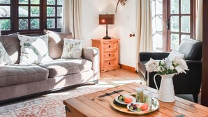 A living room with a sofa, a wooden coffee table with fruit, a vase of flowers, and a view through large windows. - 3 bedroom accommodation in Winterton-on-Sea, near Great Yarmouth (Winterton-on-Sea, near Great Yarmouth)