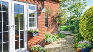 A brick house with white-framed windows, a door, and a small garden with potted plants and a pathway. - 3 bedroom accommodation in Winterton-on-Sea, near Great Yarmouth (Winterton-on-Sea, near Great Yarmouth)
