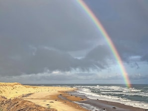 A beach with a rainbow, waves, and a cloudy sky.