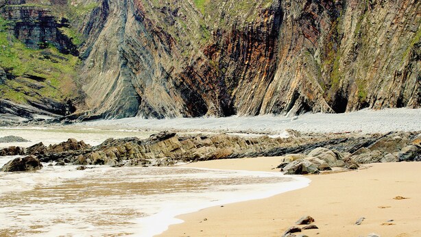 Une plage bordée d’une côte rocheuse, avec des falaises en arrière-plan.