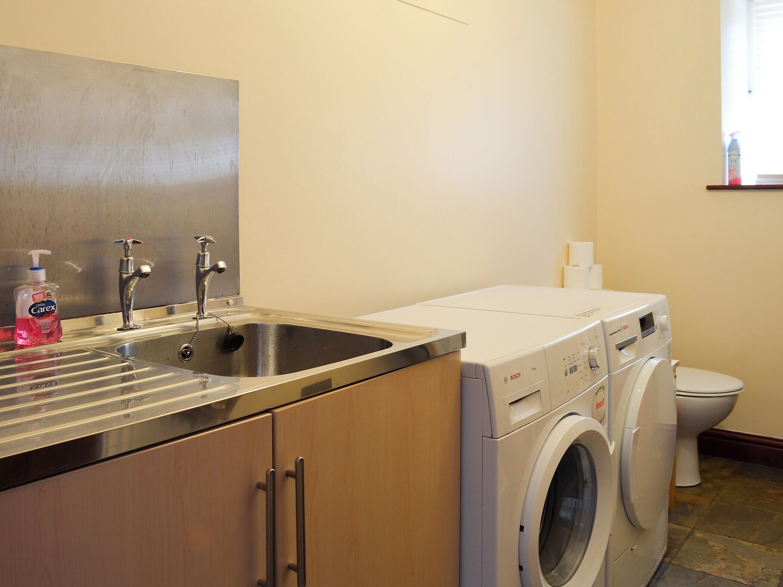 A compact laundry room with a washing machine, a sink, and a toilet.