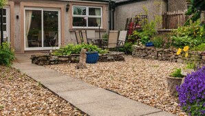 Una casa con patio, paredes de piedra, un camino de grava y diversas plantas en macetas.