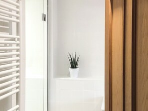 A bathroom with a white tiled wall, a potted plant, and a wooden door. - 1 bedroom accommodation in Beadnell (Beadnell)